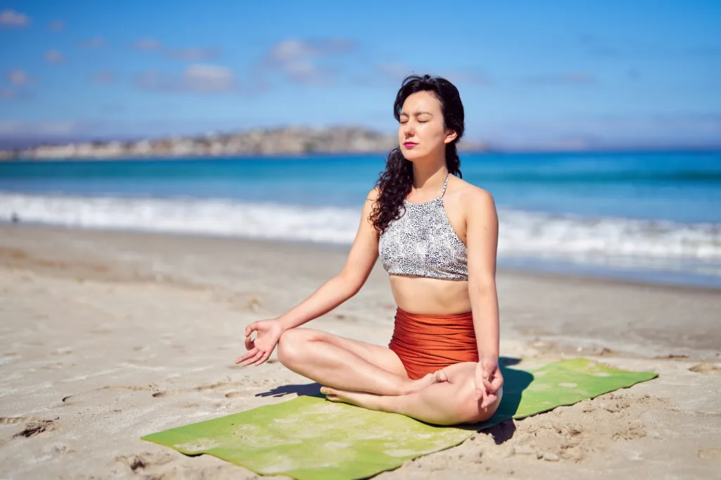 woman sitting meditating on the beach in the morning
