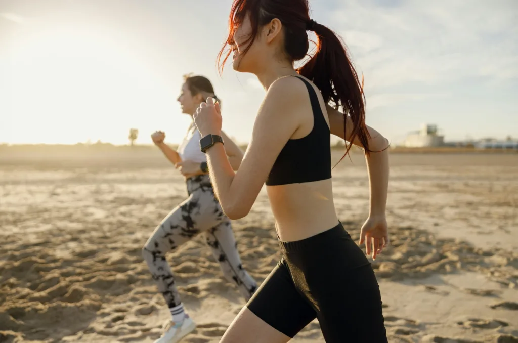 Young athletic women in sportswear is jogging along shore of beach. Concept of healthy living
